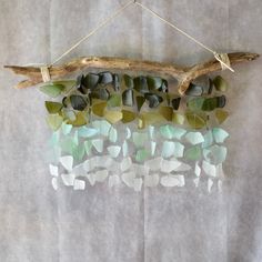 a piece of driftwood with sea glass hanging from it's side on a wall