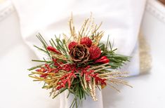 a napkin holder with pine cones and red berries on it is adorned with evergreen needles