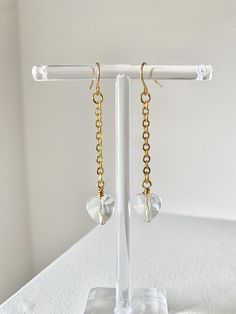 These earrings feature a gold chain with a dangling clear crystal heart. Elegant Crystal Heart Dangle Earrings, Elegant Gold Crystal Heart Earrings, Gold Crystal Heart Earrings, Gold Heart Shaped Crystal Earrings, Valentine's Day Gold Crystal Earrings, Gold Crystal Heart Shaped Earrings, Gold Heart-shaped Crystal Wedding Earrings, Gold Heart-shaped Crystal Earrings For Pierced Ears, Gold Heart-shaped Crystal Earrings