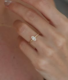 a woman's hand wearing a gold ring with a single diamond on it,