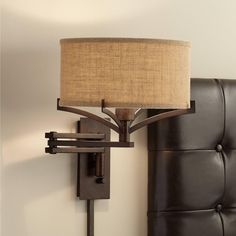 a lamp that is on the wall next to a bed with a headboard and pillows