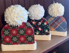 three knitted hats with pom - poms sitting on top of a shelf