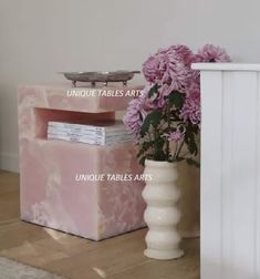 a vase with pink flowers sitting on top of it next to a white cabinet and table