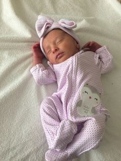 a baby is sleeping on a bed wearing a pink outfit and a bow headband