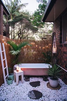 a bath tub sitting in the middle of a garden next to a wooden fence with lights on it