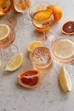 several glasses filled with different types of drinks and fruit on a table top next to oranges