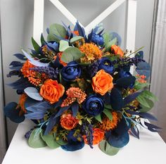 an orange and blue bouquet sitting on top of a white chair next to a window