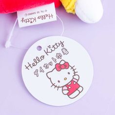 the hello kitty tag is next to a stuffed animal on a purple surface with a red and yellow teddy bear