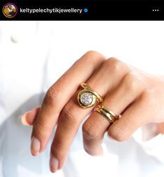 a woman's hand wearing a gold ring with a diamond in the middle and a white shirt behind her