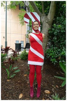 a woman dressed in a red and white striped costume standing next to a tree with a giant candy cane