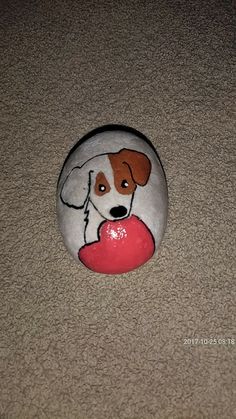 a painted rock with a dog holding a heart on it's side, sitting on the floor