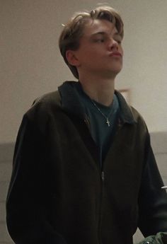 a young man standing in front of a white wall with his eyes closed and holding a remote control