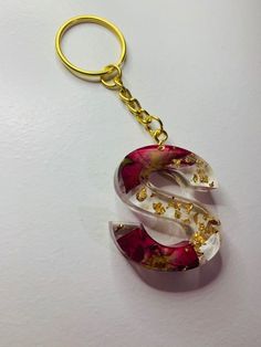 a red and white letter shaped keychain hanging from a gold - tone chain