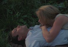 a man and woman laying on the ground in front of some tall grass, one is holding his head