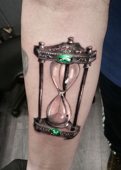 a man's leg with an hourglass tattoo on his left arm and green jewels in the middle