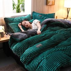 a woman laying on top of a bed covered in green comforter and pillows next to a window