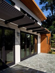 the outside of a modern home with stone patio and pergolated awnings