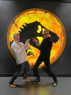 two men are dancing in front of a large yellow disk with an image of godzilla on it