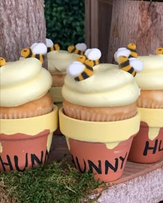 cupcakes decorated with bees sitting on top of each other in flower pots next to a tree