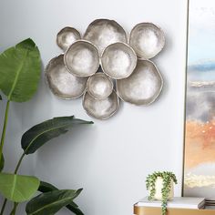 a metal plate sculpture on the wall above a table with a plant in front of it