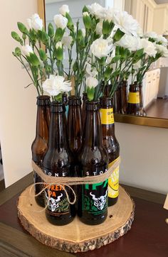 six beer bottles with white flowers in them on a wooden table next to a mirror