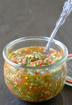 a glass jar filled with food sitting on top of a wooden table next to a spoon