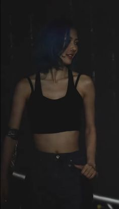 a woman with blue hair is standing in the dark and wearing a black crop top