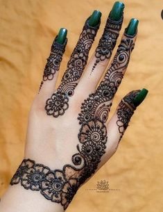 a woman's hand with henna tattoos and green nail polishes on it