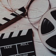 an old movie clapper, reels and glasses on a white wooden table top