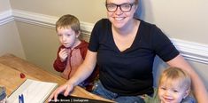 a woman sitting at a table with two children in front of her and an open laptop