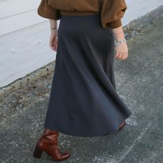 a woman walking down the street wearing a brown sweater and black skirt with high heel boots