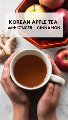 a person holding a cup of tea with ginger and cinnamon in front of some apples