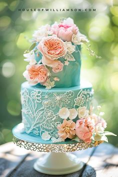 a three tiered blue cake with flowers on the top is sitting on a wooden table