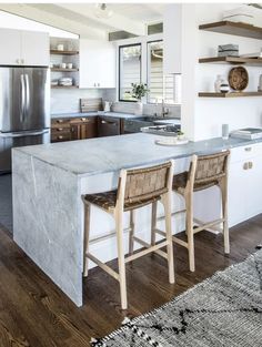 two stools sit at the center of this kitchen island with marble countertops and stainless steel appliances