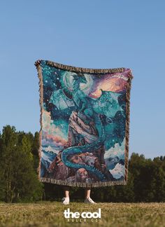 a person standing in the grass holding up a blanket with an image of a dragon on it