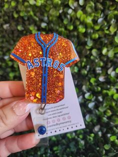 a person holding up an orange and blue baseball jersey shaped keychain with the word astros on it