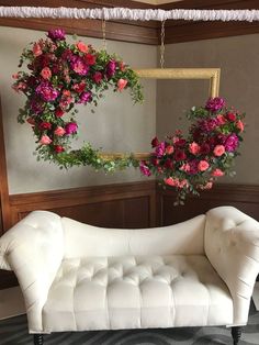 a white couch sitting in front of a mirror with flowers hanging from it's sides