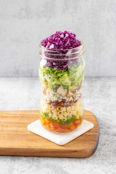 a mason jar filled with pasta salad on top of a wooden cutting board