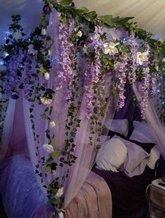 a canopy bed covered in purple flowers and greenery