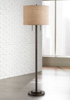 a floor lamp with a beige shade on it in front of a white brick wall