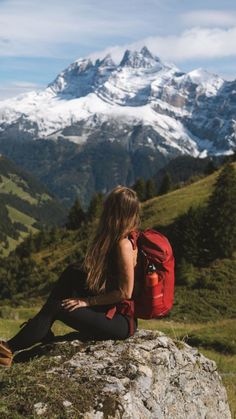 a woman sitting on top of a rock with a backpack in front of snow capped mountains