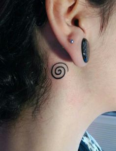 a woman's ear with a small spiral tattoo on her left behind the ear