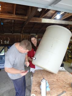 a man and woman standing next to a large white barrel on top of a wooden table