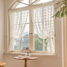 a small table and chair in front of a window with sheer curtains on the windowsill