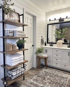 a bathroom with white cabinets and shelves filled with towels, toiletries and plants in baskets