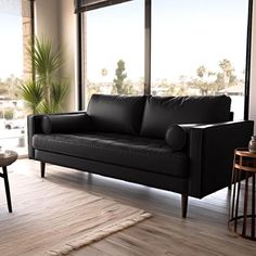 a black leather couch sitting in front of a window next to a table and chair