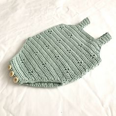 a green knitted baby bib laying on top of a white sheet with buttons