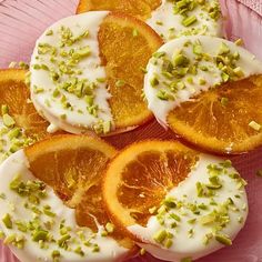 orange slices with white frosting and pistachio sprinkles on a pink plate