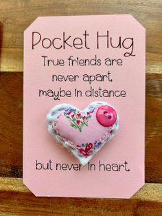 a pink heart with a button attached to it on a wooden background that says pocket hug true friends are never apart maybe in distance but