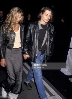 two people walking down the street at night with one person wearing a black leather jacket